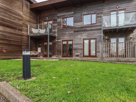 A grassy courtyard area in front of a wooden building with balconies and glass doors at Trenethick in Porthtowan