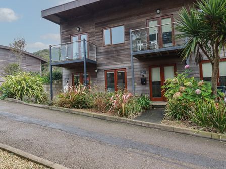 A wooden two-story building with glass balconies and plants in front at Tregullan in Porthtowan