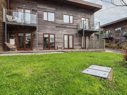 A wooden two story building with balconies chairs and glass doors in front of a grass lawn at Treveglos in Porthtowan