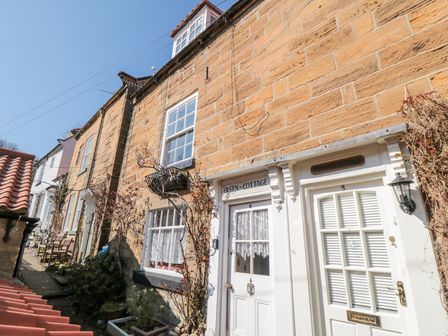 A row of stone cottages with white doors and windows on a narrow street at Olsen in Robin Hoods Bay