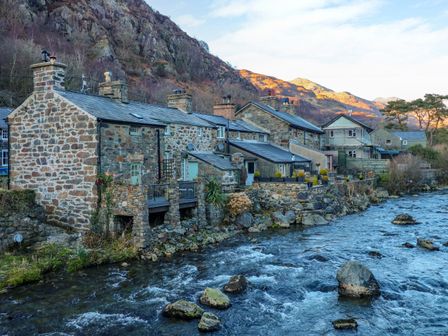 Stone houses along a river with rocky hills in the background at Llety in Beddgelert