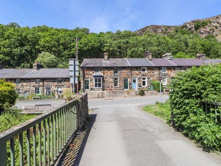 Stone cottages with slate roofs along a road with greenery and hills in the background at Llys Emrys in Beddgelert
