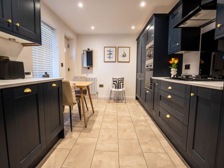 A kitchen with dark cabinets a wooden table with chairs two framed pictures and tiled floor at The Cove in Kessingland