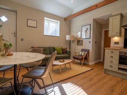 A living room with a green sofa a round marble dining table and a kitchen area at Dunes Cottage in Kessingland