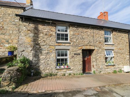 Stone cottage with slate roof two windows flower pots on sills and a wooden door at Coedmor Newport Pembrokeshire
