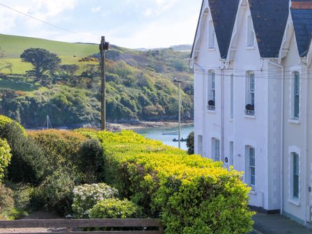 A white house with pointed roofs by a body of water with greenery and hills in the background at 2 The Elms in Salcombe