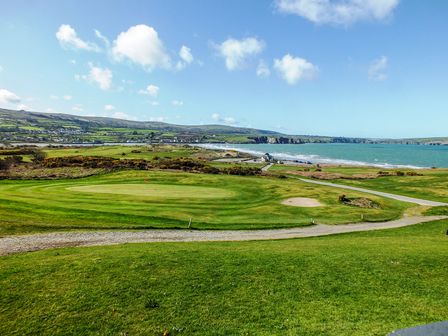 A golf course with a putting green and sand bunker near a coastal area with hills and houses in the background at Carningli Suite near Newport