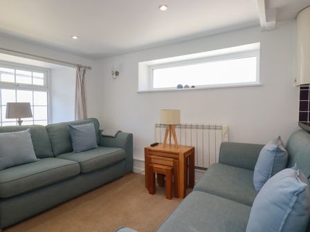 A seating area with two sofas a wooden side table with nested stools and a small lamp at St Saviours in Padstow