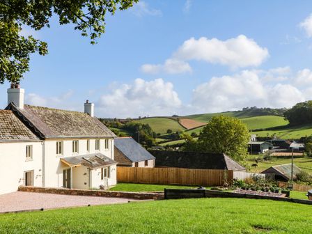 A house with a garden and hills in the background at Higher Weekaborough Farm near Ipplepen