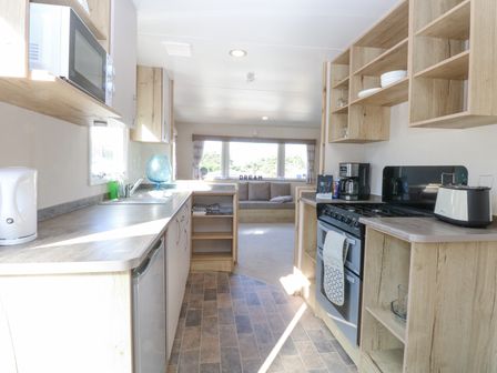 A kitchen with a stove toaster coffee maker microwave and cabinets leading to a sitting area with a sofa and large windows at 31A Foxburrow Hang in Fritton near Belton Norfolk