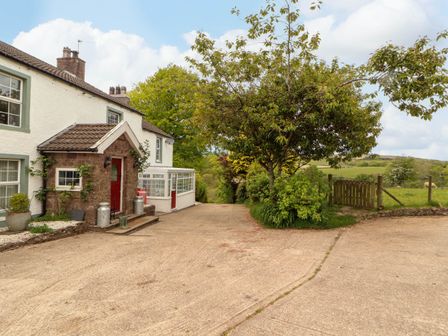 A house with a red door next to a tree and a fenced field at Kirkland Howe Cottage in Arlecdon