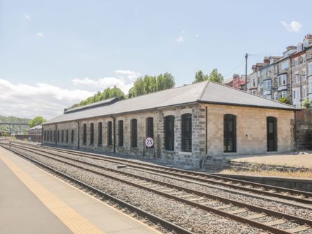 A railway platform with train tracks and a long stone building with multiple windows at Duchess of Hamilton @ Engine Shed in Whitby