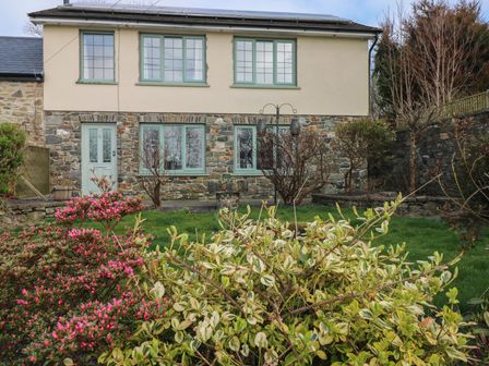 A garden with bushes and plants in front of a stone and plaster house at Carreg Yr Onnen in Penparc