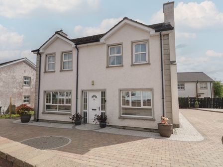 Front view of a two-story house with multiple windows and a white door with potted plants on the driveway at Donagh Cross Town House in Carndonagh County Donegal