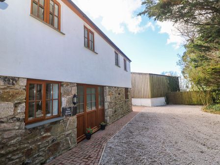 Exterior of a two-story house with wooden doors and windows gravel driveway and trees at The Baler House in Hayle