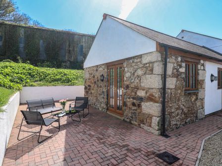 An outdoor patio area with black metal chairs and a table in front of a stone and white building at The Coach House in Hayle
