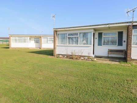 A row of single story white houses with windows and doors in a grassy area at Chalet 21 in Newport Norfolk