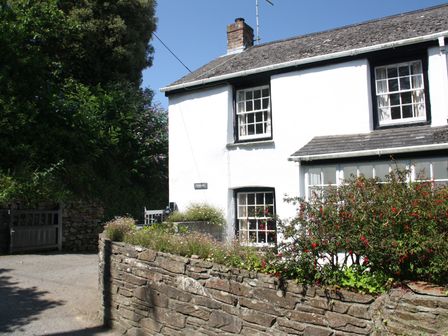 A white house with black window frames and a stone wall with plants in front at Pennine in Veryan