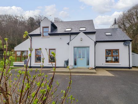 A white house with a blue front door multiple windows and a driveway at Clondallon Cottage in Clondallon near Rathmullan County Donegal