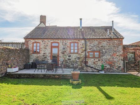A stone cottage with a tiled roof and wooden door with windows and patio furniture on a paved area at The Yarde Annexe in Pen Elm near Taunton