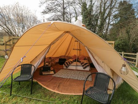 An outdoor bell tent with two black chairs on grass with a bed and rugs inside at Bell tent 4 in Camerton near Timsbury