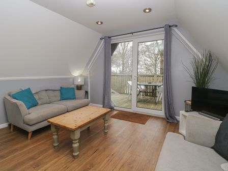 A living room with a wooden coffee table two sofas and a television near glass doors leading to a balcony at Valley Lodge 38 in St Ann's Chapel Cornwall