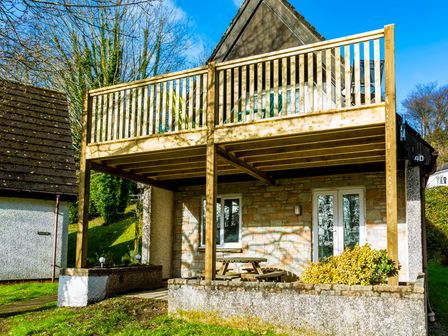 A house with a stone facade and a wooden balcony above a patio with a picnic table at Valley Lodge 40 in St Ann's Chapel Cornwall