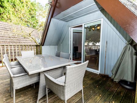 An outdoor deck area with a glass top table and six wicker chairs near a sliding door at Valley Lodge 3 in St Ann's Chapel Cornwall
