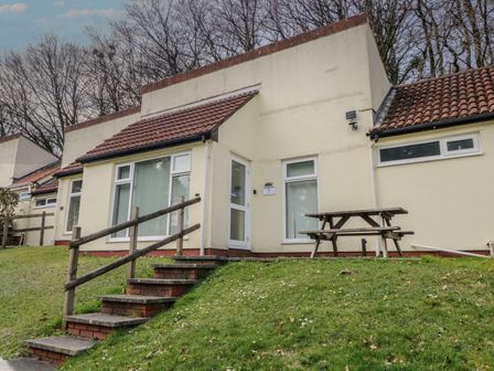 A cream colored house with tiled roof wooden railing steps and picnic table on grass at 26 Manorcombe in St Ann's Chapel Cornwall