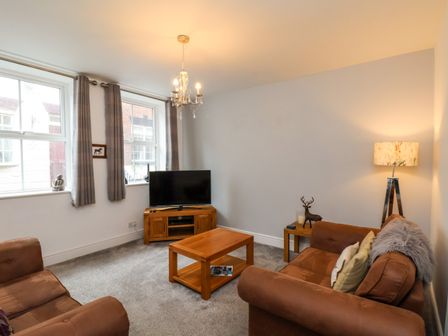 A living room with two brown sofas a wooden coffee table a TV on a wooden stand and two windows with curtains at The Bungalow in Whitby