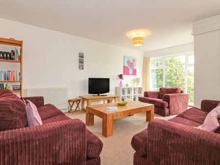 A living room with three red sofas a wooden coffee table a TV and bookshelves at Tamar Cottages 35 in St Ann's Chapel Cornwall
