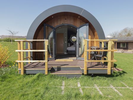 A pod with an arched roof and glass doors opening to a wooden deck with chairs and a table at The Rowan Pod in Cowbridge