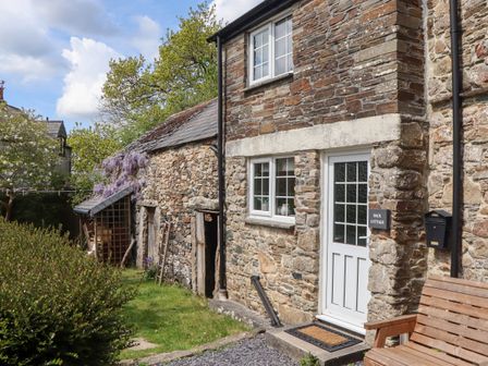 The exterior of a stone cottage with a white door and windows wooden bench and garden at Back Cottage in Walkhampton near Yelverton