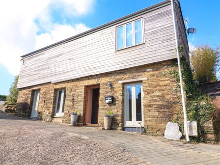 A building with stone lower walls and wooden upper walls with three doors and a window at Horsemans Barn in West Alvington near Kingsbridge