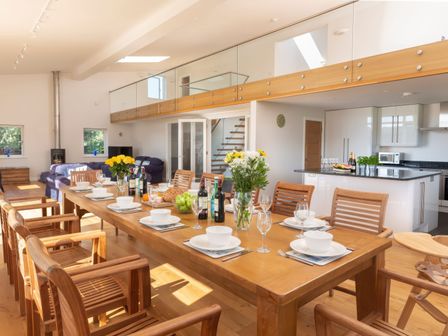 A dining area with a long wooden table set with dishes and wine bottles next to a kitchen and living room at Moult Hill Barn in Salcombe