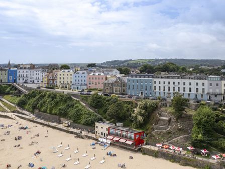 A sandy beach with people and sun loungers near a row of colorful buildings on a cliff at No 10 Croft House in Tenby
