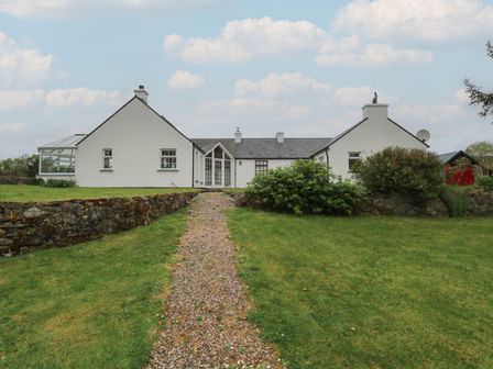 A white house with two chimneys and a gravel path leading to the front door at Teach na Realta in Frosses near Inver County Donegal