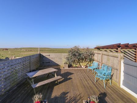 A wooden decked patio with a wooden picnic table and two blue metal chairs surrounded by wooden fencing at 48 Waxholme Road in Withernsea