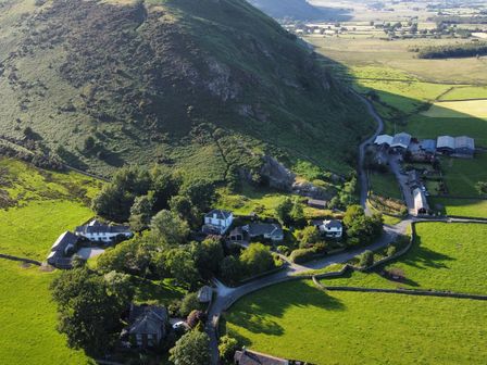 An aerial view of houses and fields near a mountain at The School at Mungrisdale in Mungrisdale near Keswick