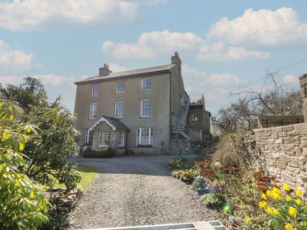 A gravel driveway leading to a three-story house with garden beds and plants on either side at Cantref House Top Floor in Brecon