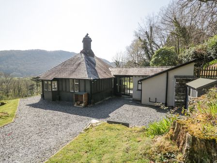A cottage with a gravel driveway and surrounding trees and hills at Bwthyn y Coediwr The Woodcutters Cottage in Tan Y Bwlch Maentwrog