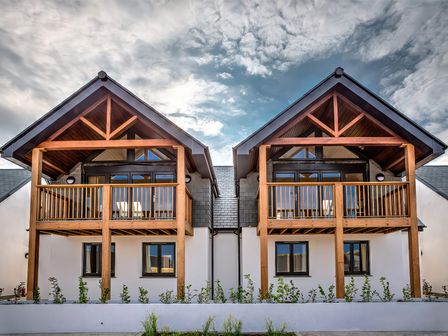 Two modern houses with wooden balconies and triangular roofs under a cloudy sky at Villa 4 in Mullion