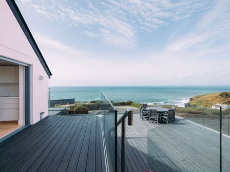 A deck with outdoor furniture overlooking the ocean with a glass railing at Shearwater in Mullion