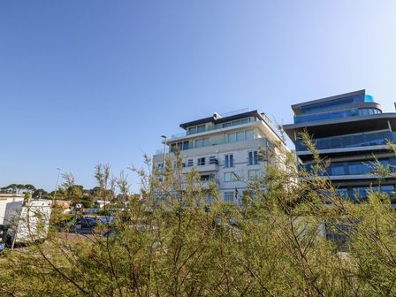 Modern apartment buildings with balconies behind trees under a clear sky at Flat 7 Sand Acres in Canford Cliffs