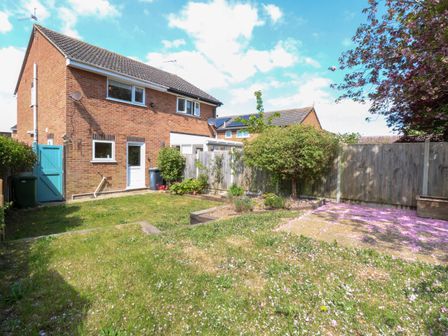 A backyard garden with grass a tree and a wooden fence behind a brick house at Sweetacres in Hemsby
