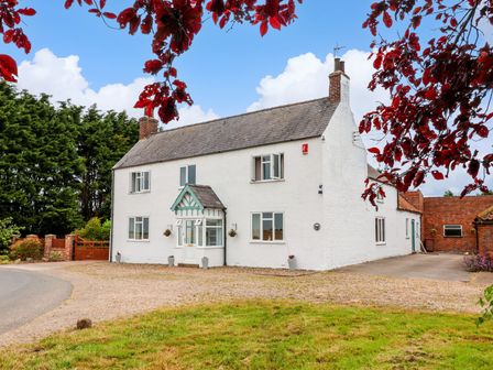 A white two-story house with a small porch and gravel driveway framed by red leaves at Bewholme in Skipsea