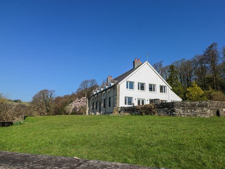 A white two-story house with multiple windows surrounded by green grass and trees at Coytrahen House Coytrahen near Bettws