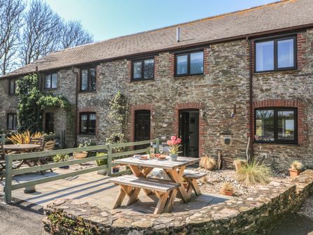 A stone cottage with outdoor wooden picnic table and benches with flowers and drinks at Tinkers Cottage in Bigbury