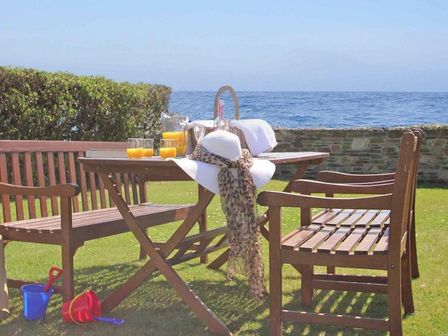 A wooden outdoor table and benches on grass with orange juice glasses and a sunhat near the sea at Watchtower Downderry near Looe