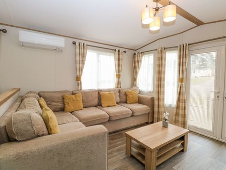 A living room with a beige sectional sofa and yellow cushions with a wooden coffee table and windows with plaid curtains at 75 Foxburrow Hang in Fritton